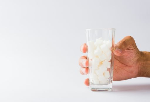 Hand hold on glass full of white sugar cube sweet food ingredient, isolated on white background, health high blood risk of diabetes and calorie intake concept and unhealthy drink