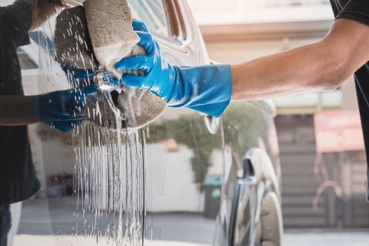 Car wash staff wearing blue rubber gloves using a sponge moistened with soap and water to clean the car.