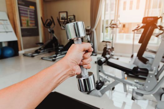 Closeup a man's hand holds a dumbbell with his left hand in the gym, Concept for exercise and health care.