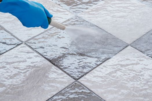 Hand of man wearing blue rubber gloves using a hose to cleaning the tile floor.