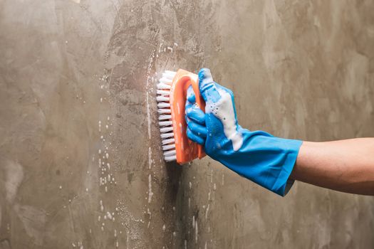 Closeup hand wearing blue rubber gloves is used to convert scrub cleaning on the concrete wall.