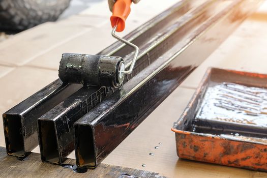 The painter wears cloth gloves, using a black paint roller on the steel rod.