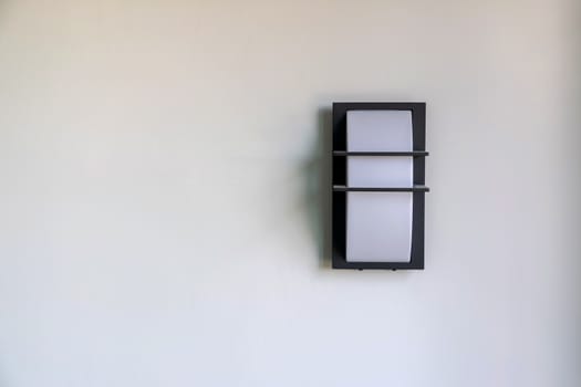 Close-up of a modern design of a wall mounted house lighting on white cement walls.