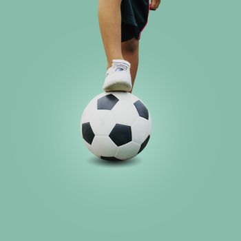 Closeup feet of a boy wearing white sneakers stepping on a soccer ball isolated on pastel color background, with clipping path.
