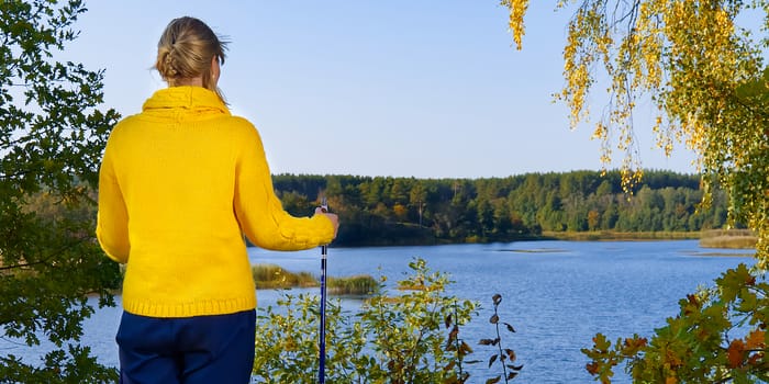 Woman in yellow sweater and Trekking pole looking at the lake after hike on a sunny day. hiking concept, outdoor lifestyle.