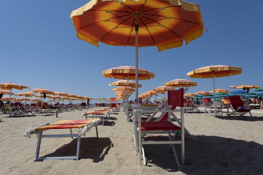 A lot of orange white sun umbrellas on a beach, with a view of a horizon line over the sea, sky, a symbol for holiday vacation