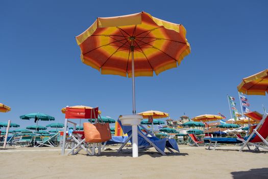 A lot of orange white sun umbrellas on a beach, with a view of a horizon line over the sea, sky, a symbol for holiday vacation