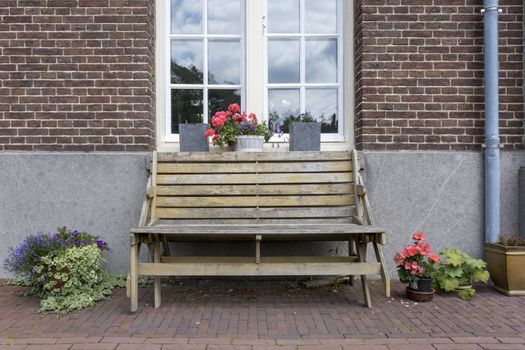 Front view of a wooden bench in front of a house with reflections in the window with flowers