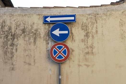 Old blue metallic arrow sign against a damaged concrete wall indicating to go left and no parking sign - concept image