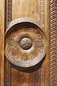 Detail of old wooden door with metal handle on board with carved pattern. Dark brown solid front door in vintage and antique style. Exterior and facade.