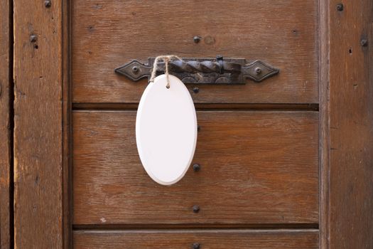 Antique door handle on a wooden door with a white sign hanging on a door.
