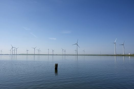 Modern windmills in the water near the shore along a green grassy dike in the netherlands