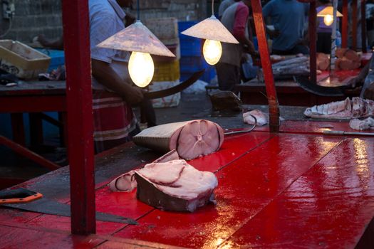 Negombo, Sri Lanka - July 25, 2018: A dead fish cut into pieces under lamps at the early morning fish market