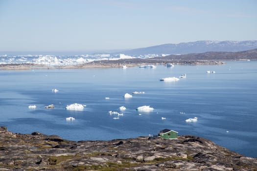 Ilulissat, Greenland - July 08, 2018: A green wooden house at the coast with icebergs in the background.