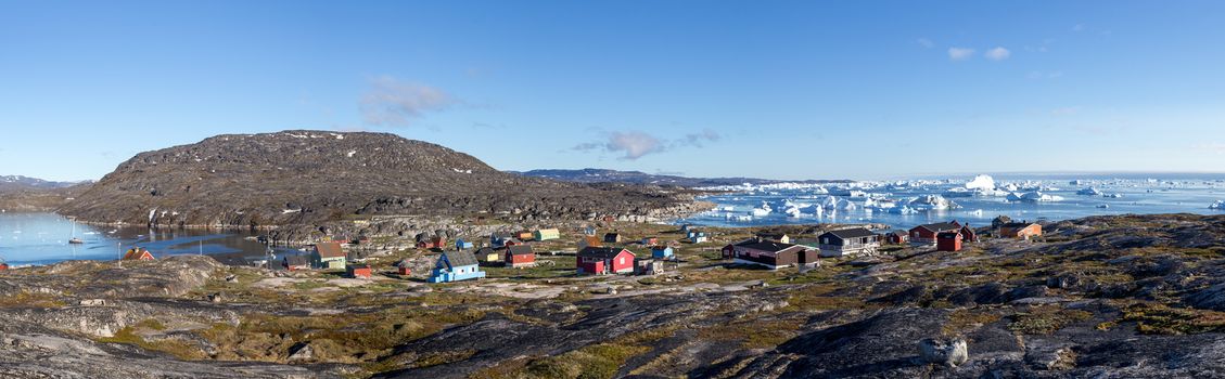 Rodebay, Greenland - July 09, 2018: Colorful wooden houses with icebergs in the background. Rodebay, also known as Oqaatsut is a fishing settlement north of Ilulissat.