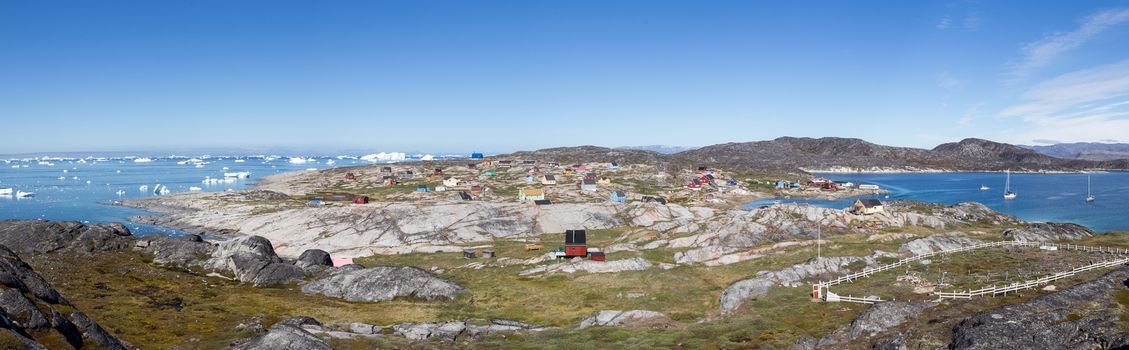 Rodebay, Greenland - July 09, 2018: Colorful wooden houses with icebergs in the background. Rodebay, also known as Oqaatsut is a fishing settlement north of Ilulissat.