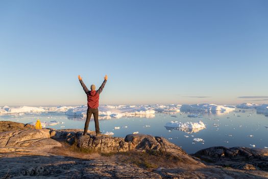 Ilulissat, Greenland - July 7, 2018: Young man looking at the Ilulissat Icefjord during midnight sun. Ilulissat Icefjord was declared a UNESCO World Heritage Site in 2004.
