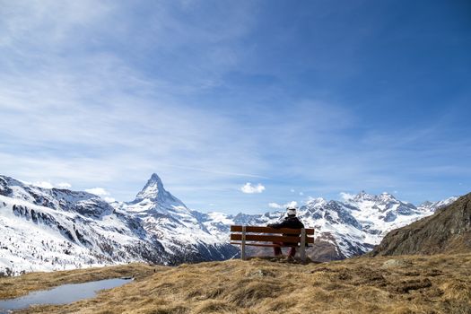 An unrecognisable man on a bench with view of the famous Matterhorn.