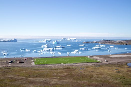 Qeqertarsuaq, Greenland - July 6, 2018: Soccer field with the ocean and icebergs in the background