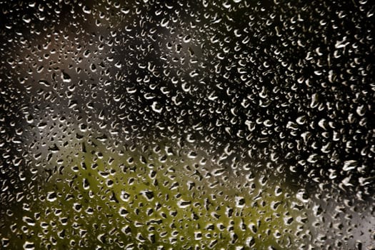 drops of water in the window on rainy day and street at the background