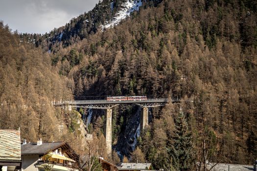 Zermatt, Switzerrland - April 11, 2017: A red train crossing an arch bridge in Zermatt