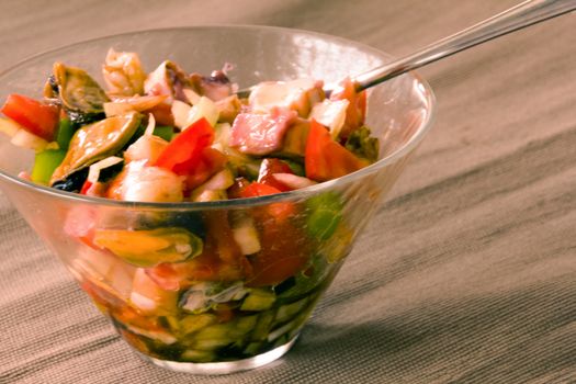 transparent bowl full of shellfish and vegetables salad and fork on the tablecloth