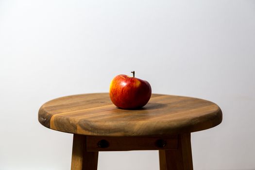 Photography of a single red apple on a wooden stool.