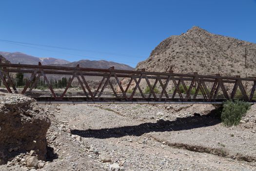 Photograph of a steel bridge construction over a dry river bed in Tilcara, Argentina.