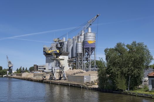 Bulk-handling crane unloading sand, road metal and gravel from cargo vessel ship, heavy vehicle and portal crane loader working with bulk materials in dock terminal