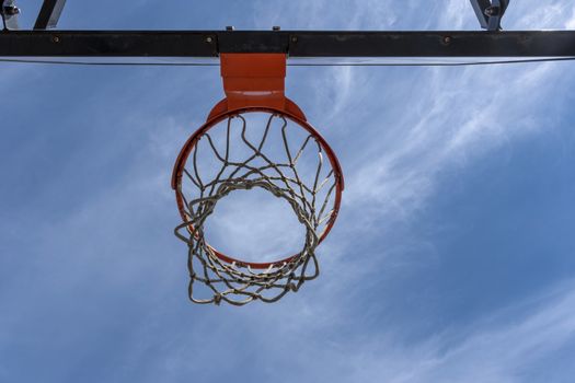 A photo from a low angle of a basketball hoop with a red ring against a cloudless warm summer sky