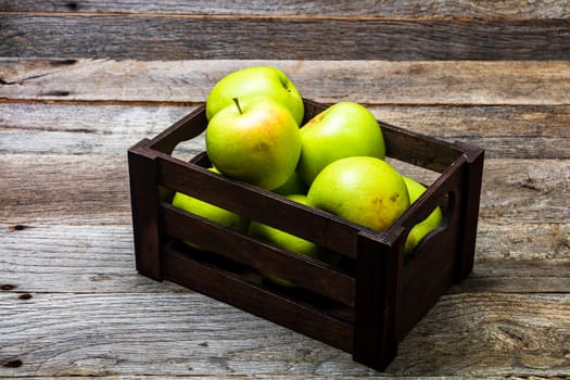 Wooden crate with ripe green apples on wooden table.