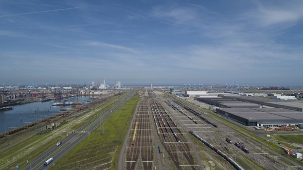 Aerial bird view photo of railroad container terminal with train loaded with containers by overhead crane also showing classification yard and heavy industry in background