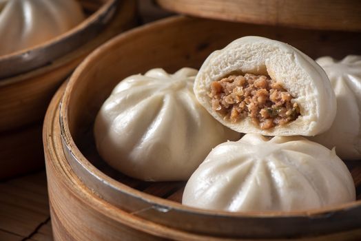 Delicious baozi, Chinese steamed meat bun is ready to eat on serving plate and steamer, close up, copy space product design concept.