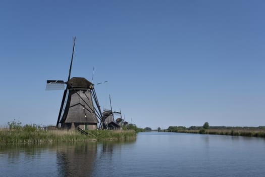 Landscape with beautiful traditional dutch windmills near the water canals with blue sky and clouds reflection in water. Kinderdijk