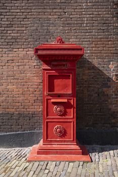 red old Dutch mailbox standing against a brick wall