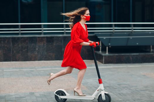 Young woman with electric scooter in red dress and gloves with face mask at the city. New normal fashion and coronavirus COVID protection concept