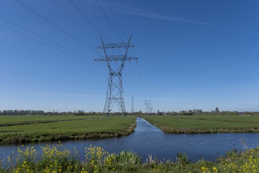 High voltage lines and power pylons in a flat and green agricultural landscape on a sunny day with cirrus clouds in the blue sky