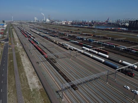 Aerial bird view photo of railroad container terminal with train loaded with containers by overhead crane also showing classification yard and heavy industry in background