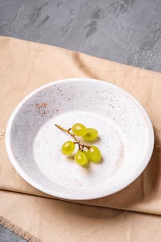 Fresh ripe white grape berries in wooden bowl on linen tablecloth, stone concrete background, angle view