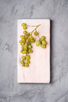 Fresh ripe white grape berries on wooden cutting board, stone concrete background, top view