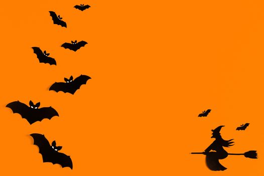 Silhouettes of a flock of bats and a witch flying on a broom made of black paper on an orange background. Halloween greeting template with copy space. Flat lay for your design. ready-made template.