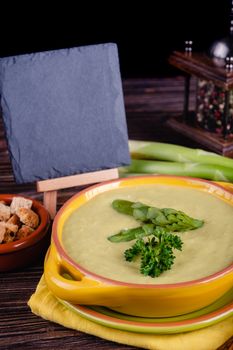 Fresh asparagus creamy soup and ingredients on wooden table on rustic wooden background, selective focus