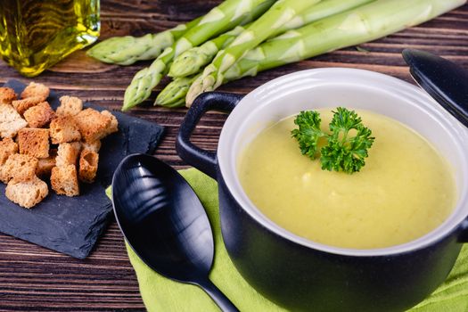 Fresh asparagus creamy soup and ingredients on wooden table on rustic wooden background, selective focus