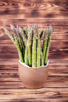 Asparagus in earthen bowl on rustic wooden background.