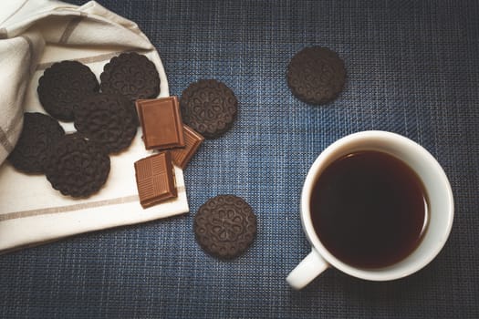 Brown cookies and chocolate lying next to coffee in a white cup