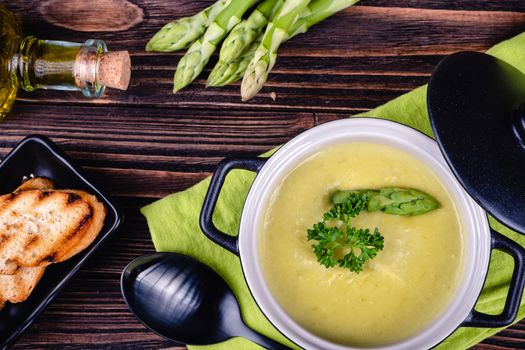 Fresh asparagus creamy soup and ingredients on wooden table on rustic wooden background, selective focus