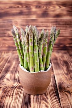 Asparagus in earthen bowl on rustic wooden background.