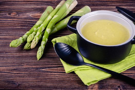 Fresh asparagus creamy soup and ingredients on wooden table on rustic wooden background, selective focus