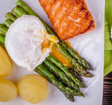 Green asparagus and boiled poached egg on a white plate over a wooden background. selective focus.