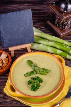 Fresh asparagus creamy soup and ingredients on wooden table on rustic wooden background, selective focus